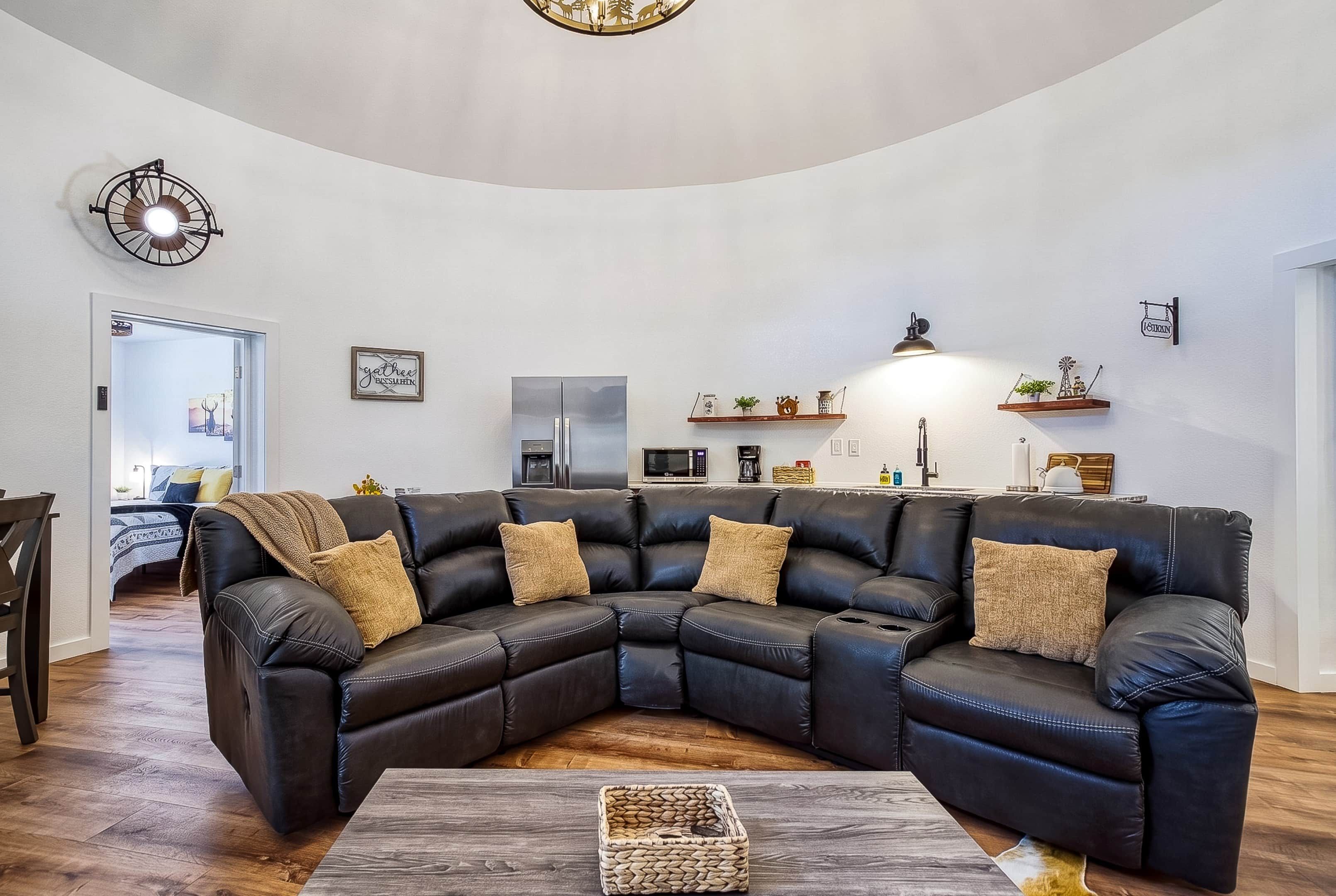 A modern living room with a sectional sofa, a coffee table, and a kitchen area in the background.