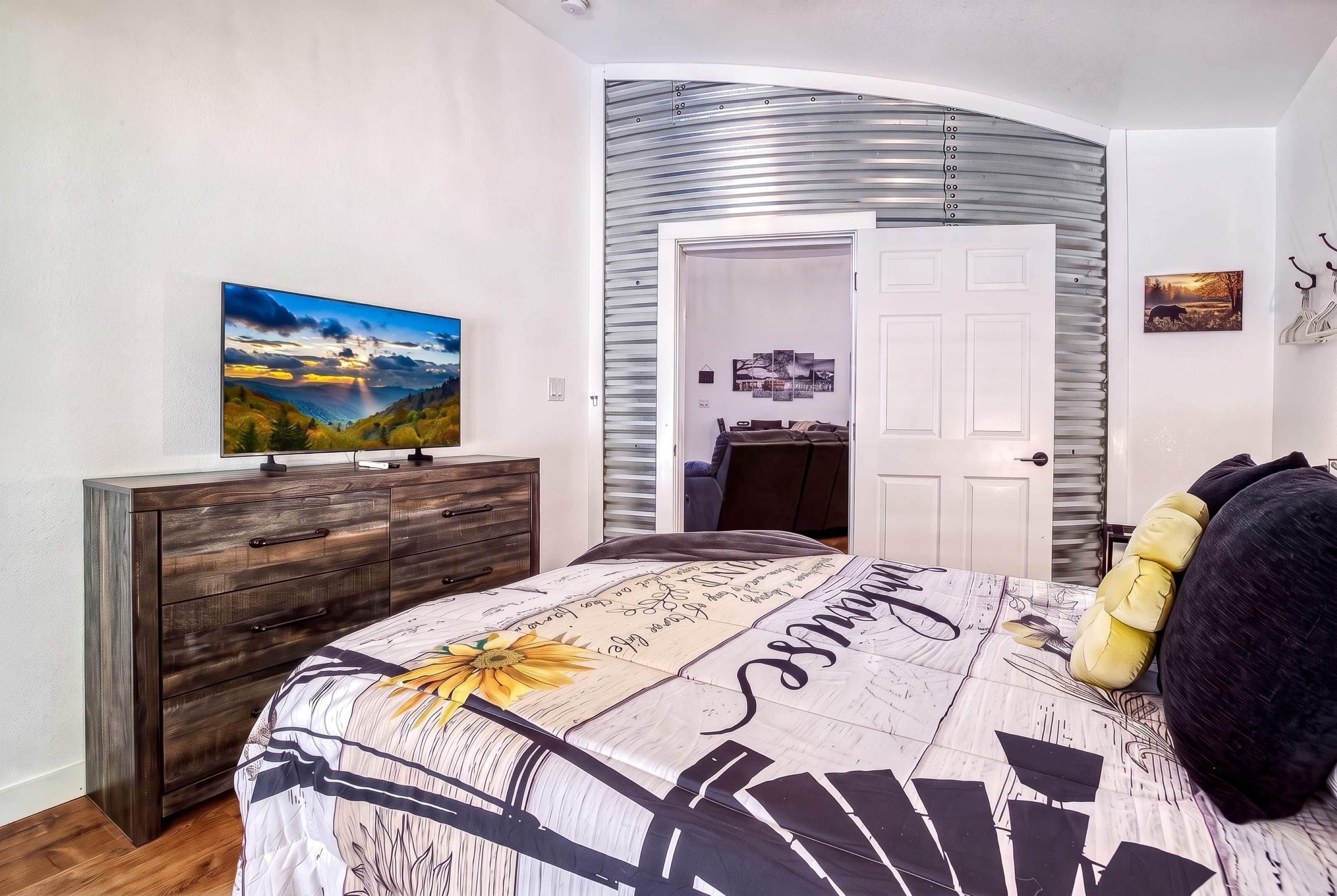 A bedroom with a bed, a dresser, a painting, and a door leading to another room.