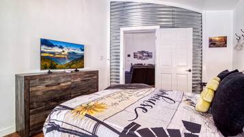 A bedroom with a bed, a dresser, a painting, and a door leading to another room.
