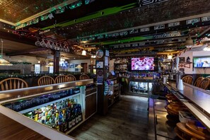 A bar with multiple seating areas, a television screen, and a variety of bottles and glasses on shelves. - Room 1 - Queen (Palmerton)