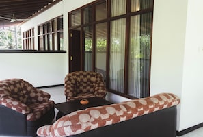Una habitación con sofá, sillas, una mesita y ventanas amplias con cortinas.