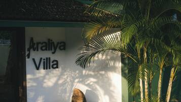Señal para 'Araliya Villa' con un paisaje tropical que incluye palmeras y rocas.
