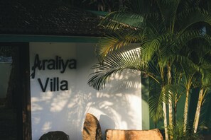 Señal para 'Araliya Villa' con un paisaje tropical que incluye palmeras y rocas.