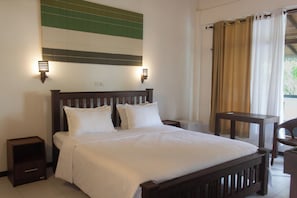 Una cama bien hecha con cabecera de madera, dos lámparas de noche, una mesita y una silla en una habitación de hotel.