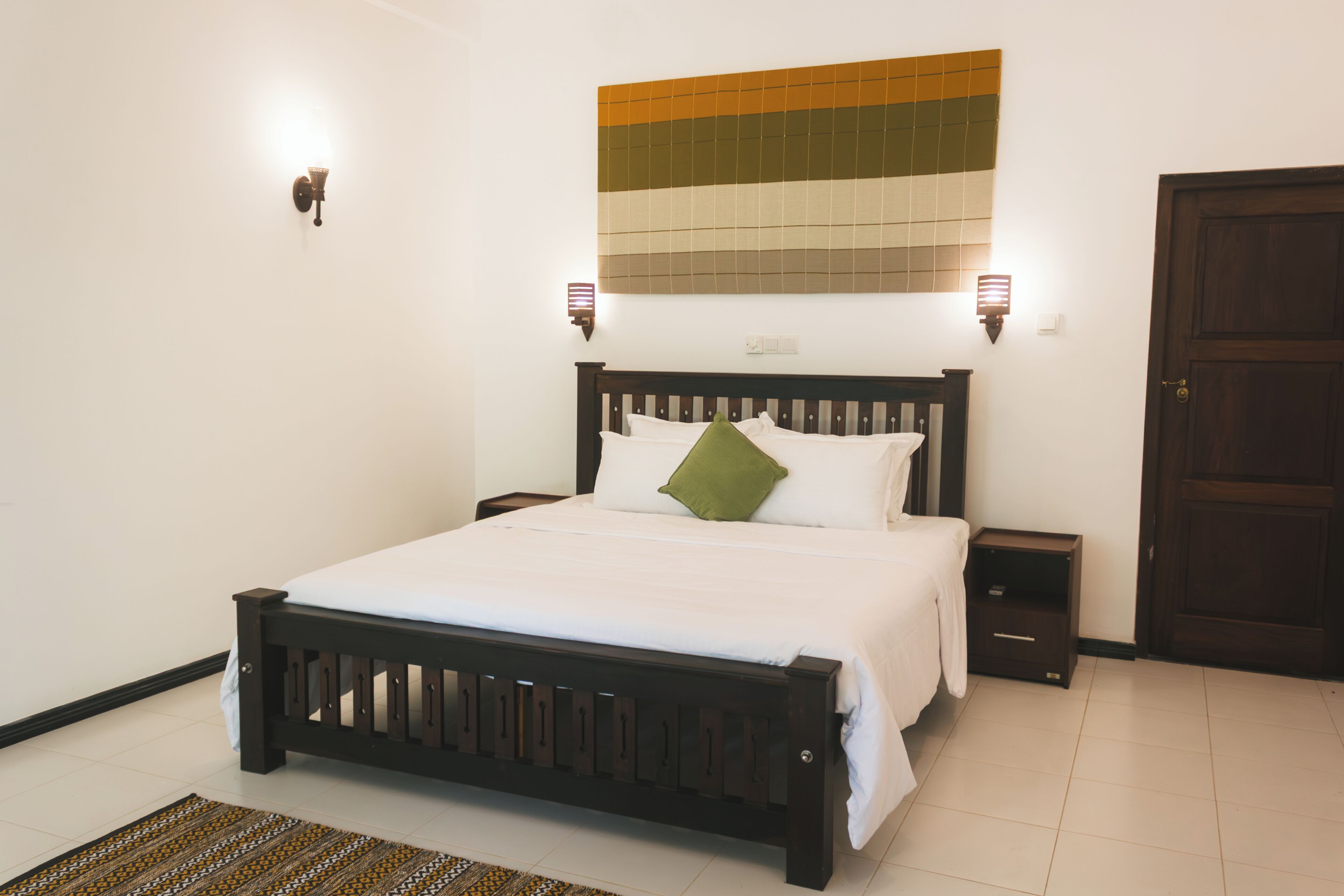 Una cama bien hecha con estructura de madera, dos mesitas de noche y un aplique de pared.
