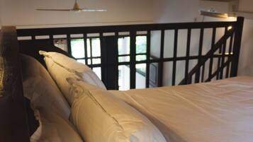 A bed with white linens and a wooden headboard in a room with a sloped ceiling and a window with a view.