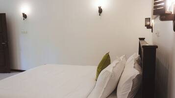 Una cama con ropa blanca y un cabecero de madera, dos lámparas de pared y una puerta a la izquierda.