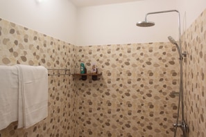 Un espacio de ducha con ducha de lluvia, una toalla colgada en un perchero y un estante con artículos de aseo.