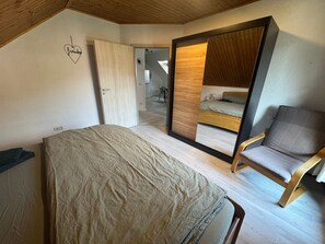 A bedroom with a bed, a chair, a wardrobe, and a mirror.