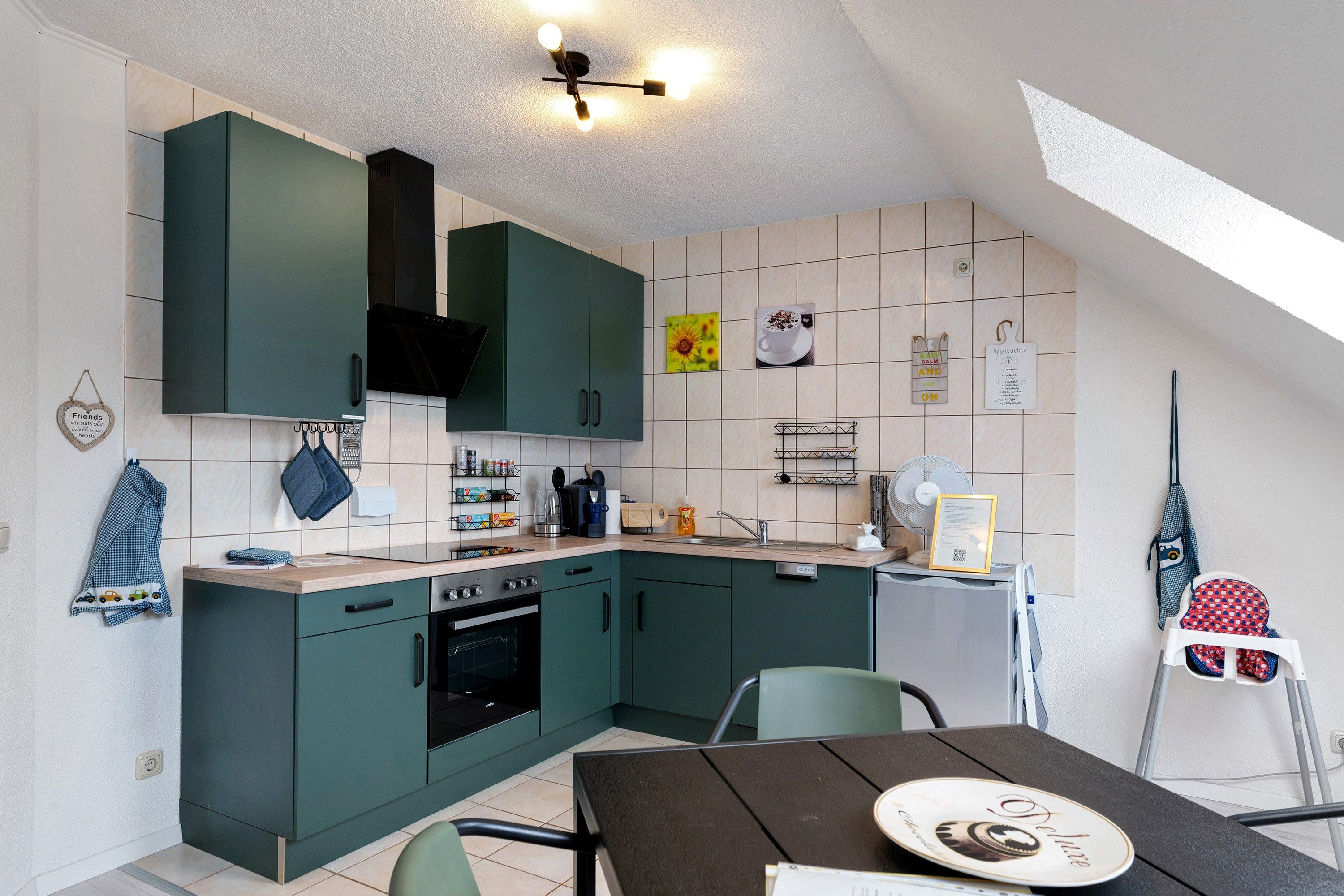 Eine kleine Küche mit grünen Schränken, einem eingebauten Backofen, einem Esstisch mit Teller und einem Deckenventilator.