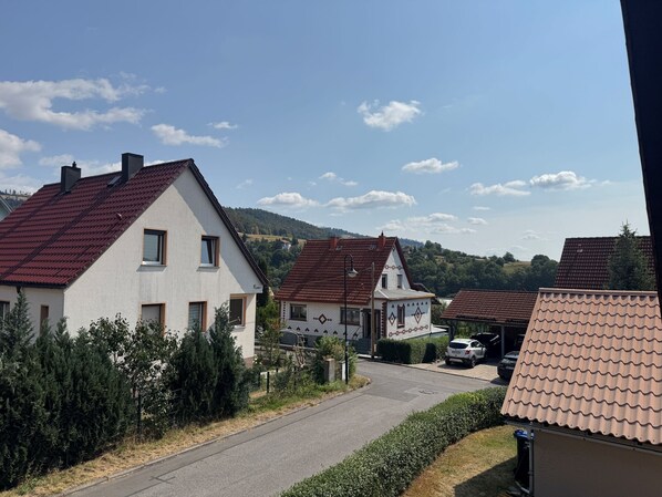 A residential street with houses, a clear sky, and a hilly landscape in the background.