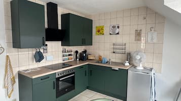 Une cuisine avec des meubles de couleur verte, une hotte noire, un four encastré, un évier et un réfrigérateur.