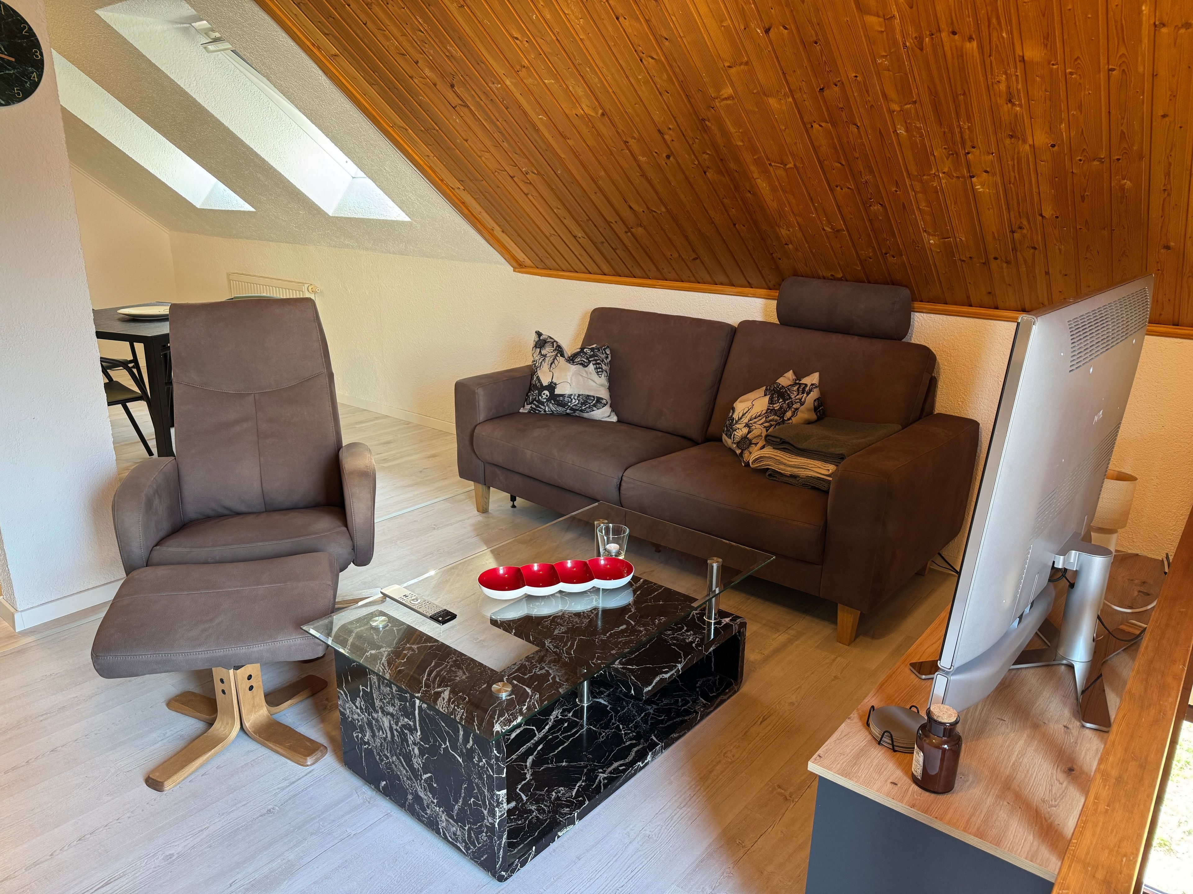 Un salon moderne avec un canapé en cuir marron, une table basse en verre et un téléviseur.