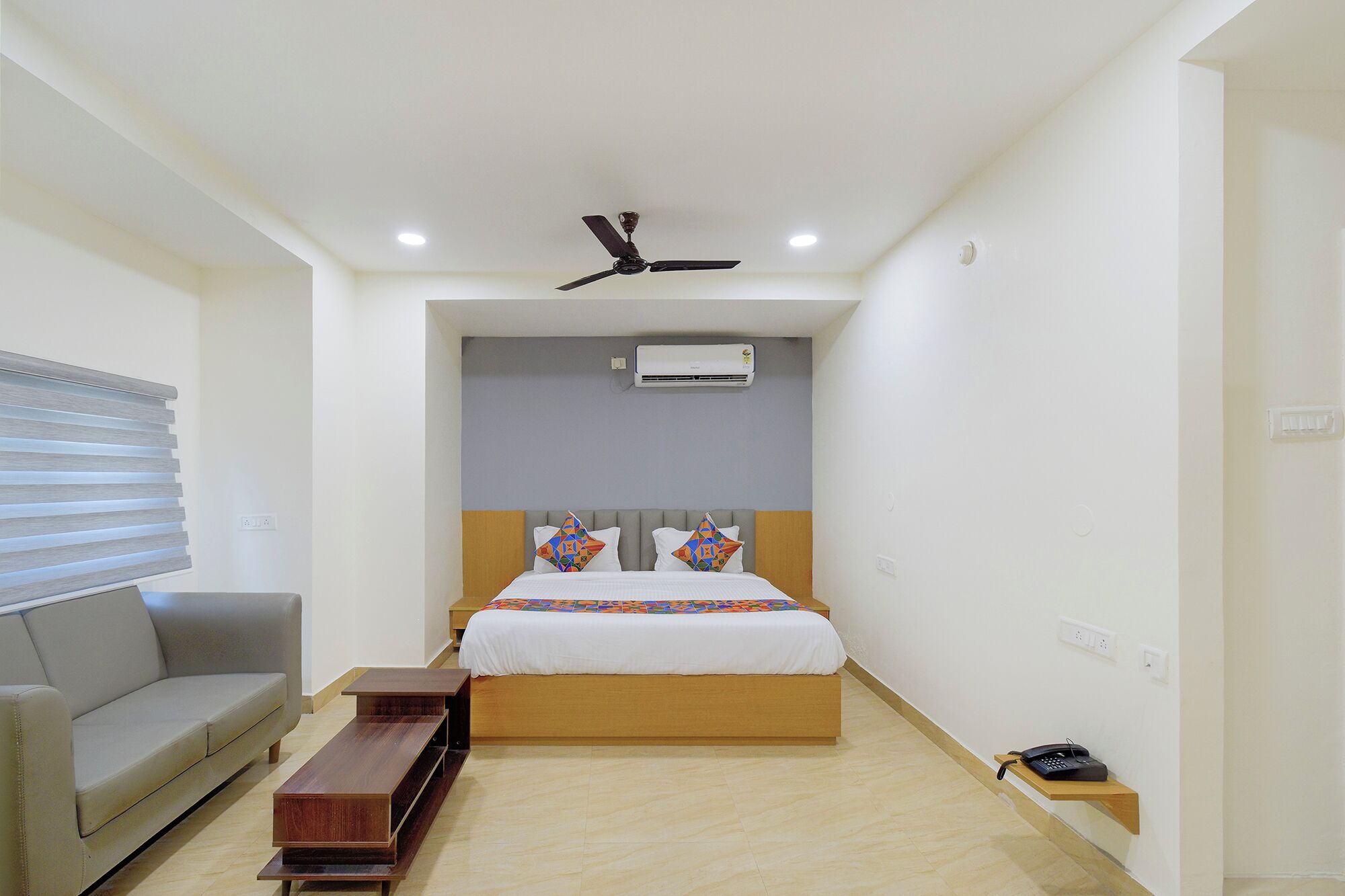 Ein Hotelzimmer mit Bett, Sofa, Nachttisch aus Holz, Deckenventilator, Klimaanlage und Telefon.