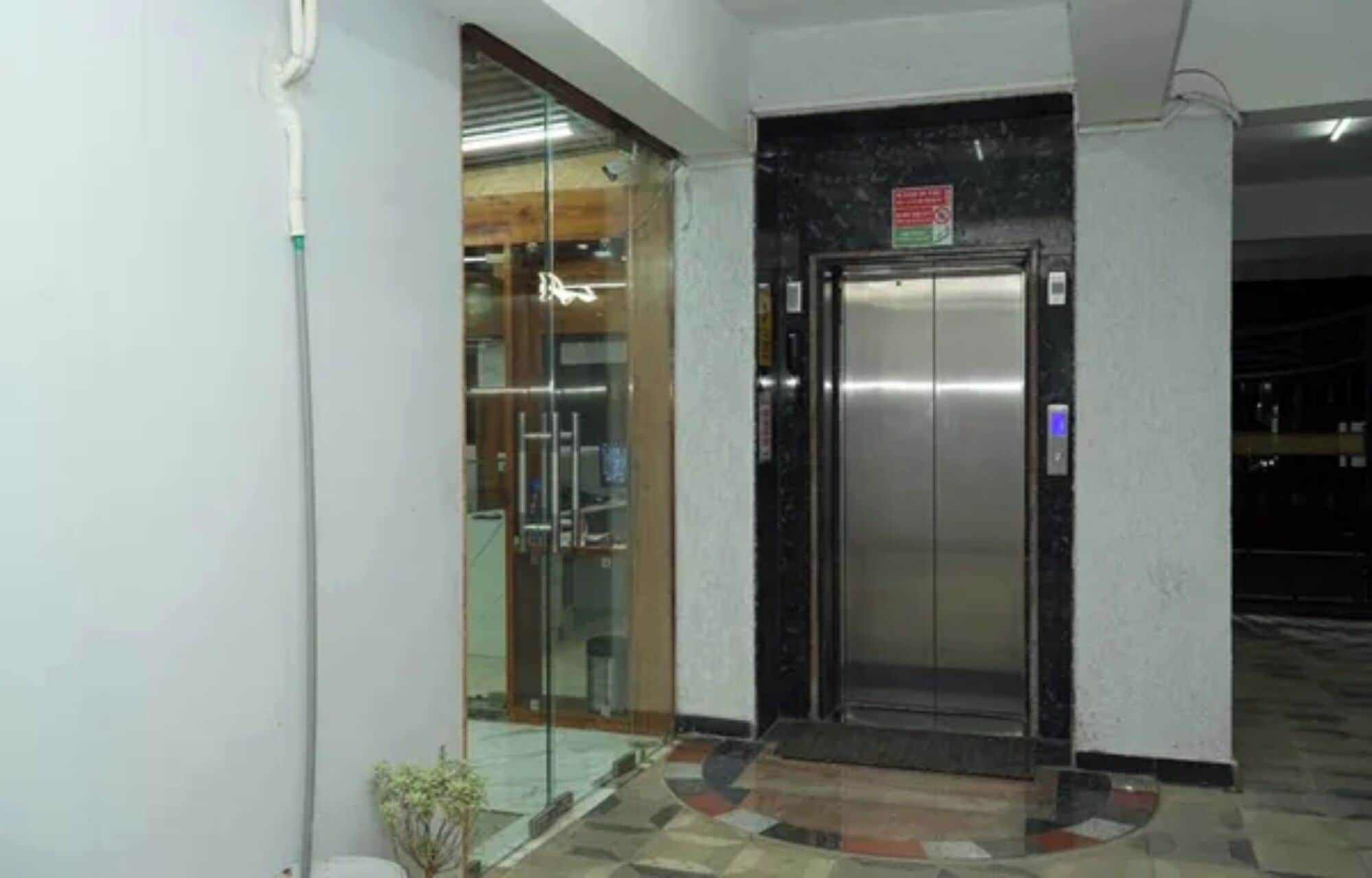 Un ascensor con pantalla digital, puerta de cristal y piso de baldosas.