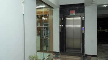 Un ascensor con pantalla digital, puerta de cristal y piso de baldosas.