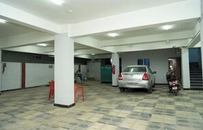A parking garage with a car and a motorcycle, white pillars, and a tiled floor.