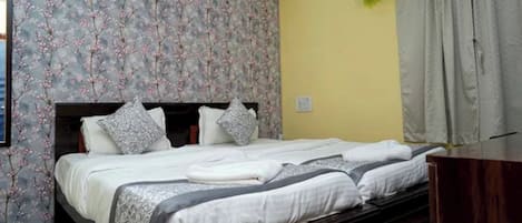 Una cama bien hecha con almohadas y una manta, un cabecero con estampado floral y un aparador de madera.