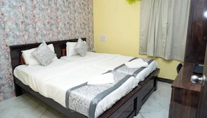 Una cama bien hecha con almohadas y una colcha, cabecera de madera, cómoda de madera y un estampado floral en el papel tapiz.