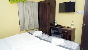 A hotel room with a bed, a desk, a wardrobe, a television, and a window with curtains.