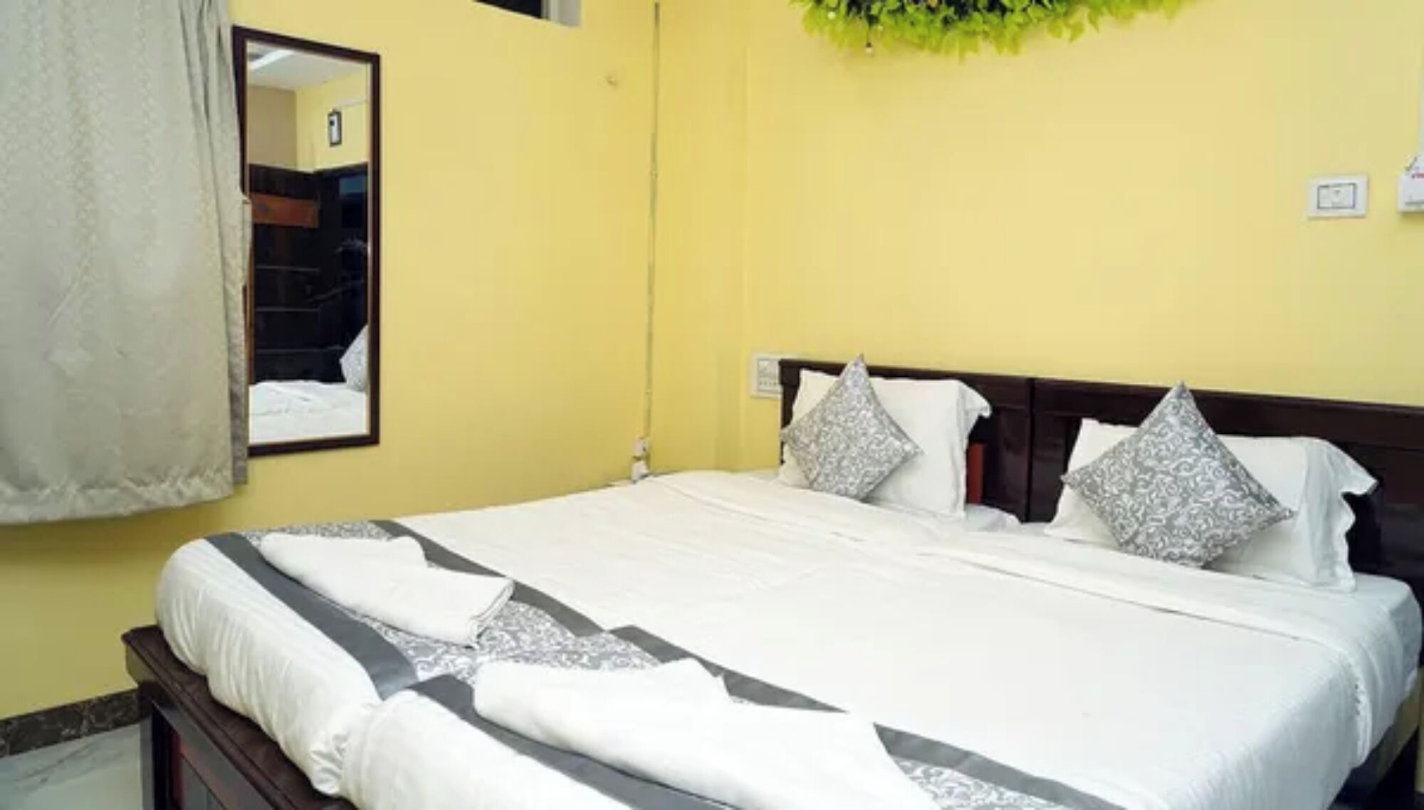 A hotel room with a bed, a mirror, and a wall-mounted light fixture.