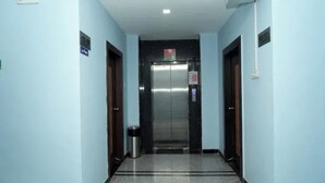 A hallway with a central elevator, light blue walls, and a tiled floor.
