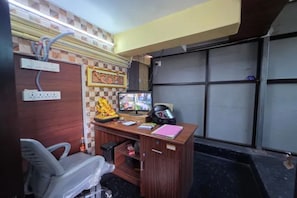 A room with a desk, chair, and a television. There are electrical outlets and a helmet on the desk. - Fabhotel Ar Residency Ii (Tiruvannamalai)