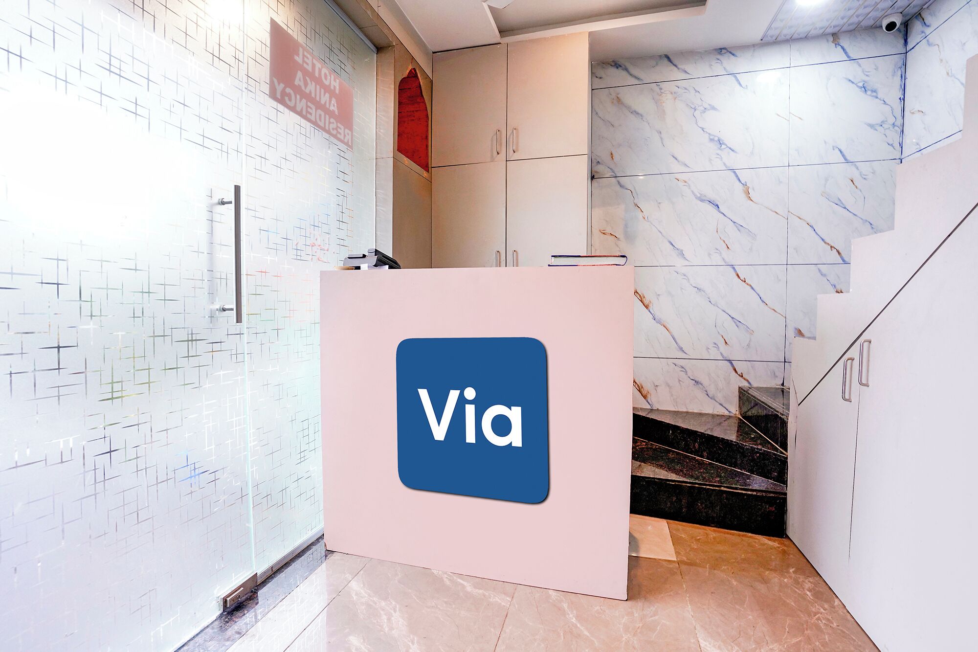 A reception desk with a 'Via' logo, a tiled wall with a geometric pattern, and a marble floor.