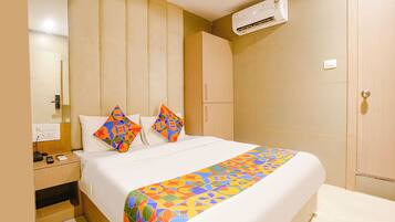 A hotel room with a bed, a bedside table, an air conditioning unit, and a wardrobe.