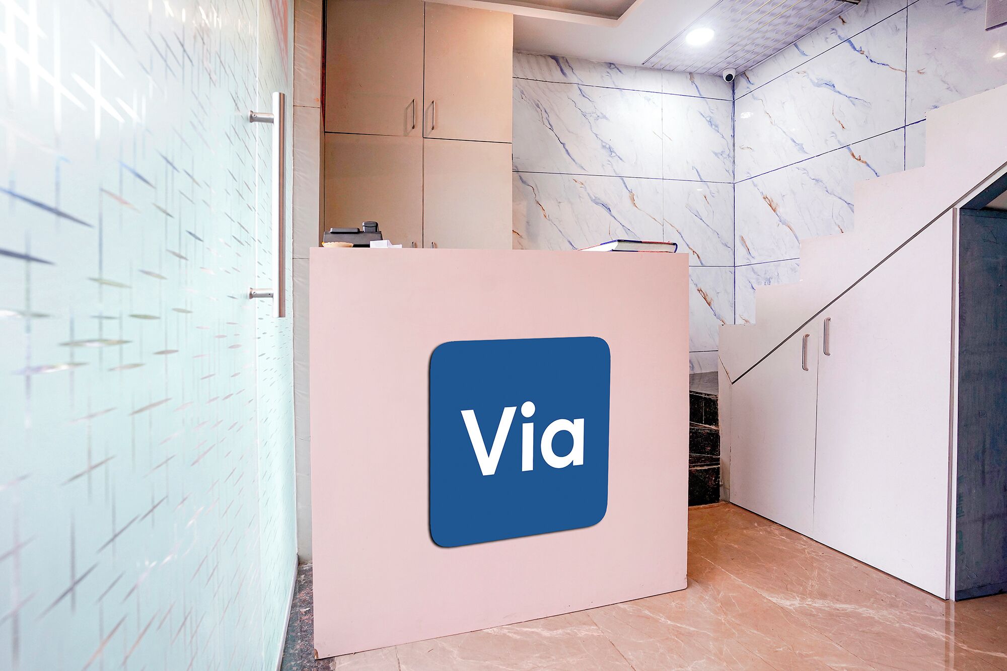 A reception area with a blue logo on a pink counter, marble walls, and a staircase.