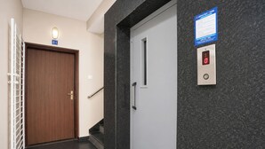 A hallway with a wooden door, a white door with a handrail, and a wall-mounted elevator control panel.
