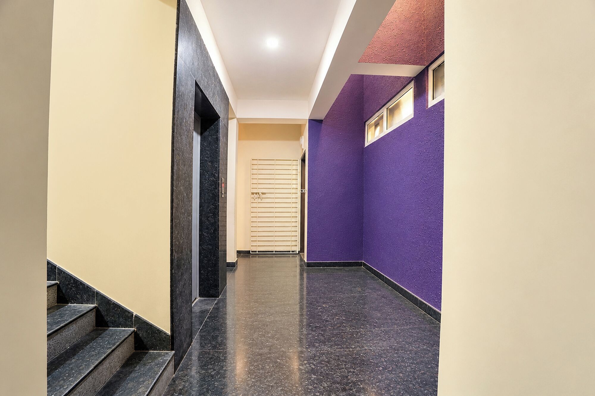 A hallway with a staircase, a door with a metal gate, and walls painted in two colors.