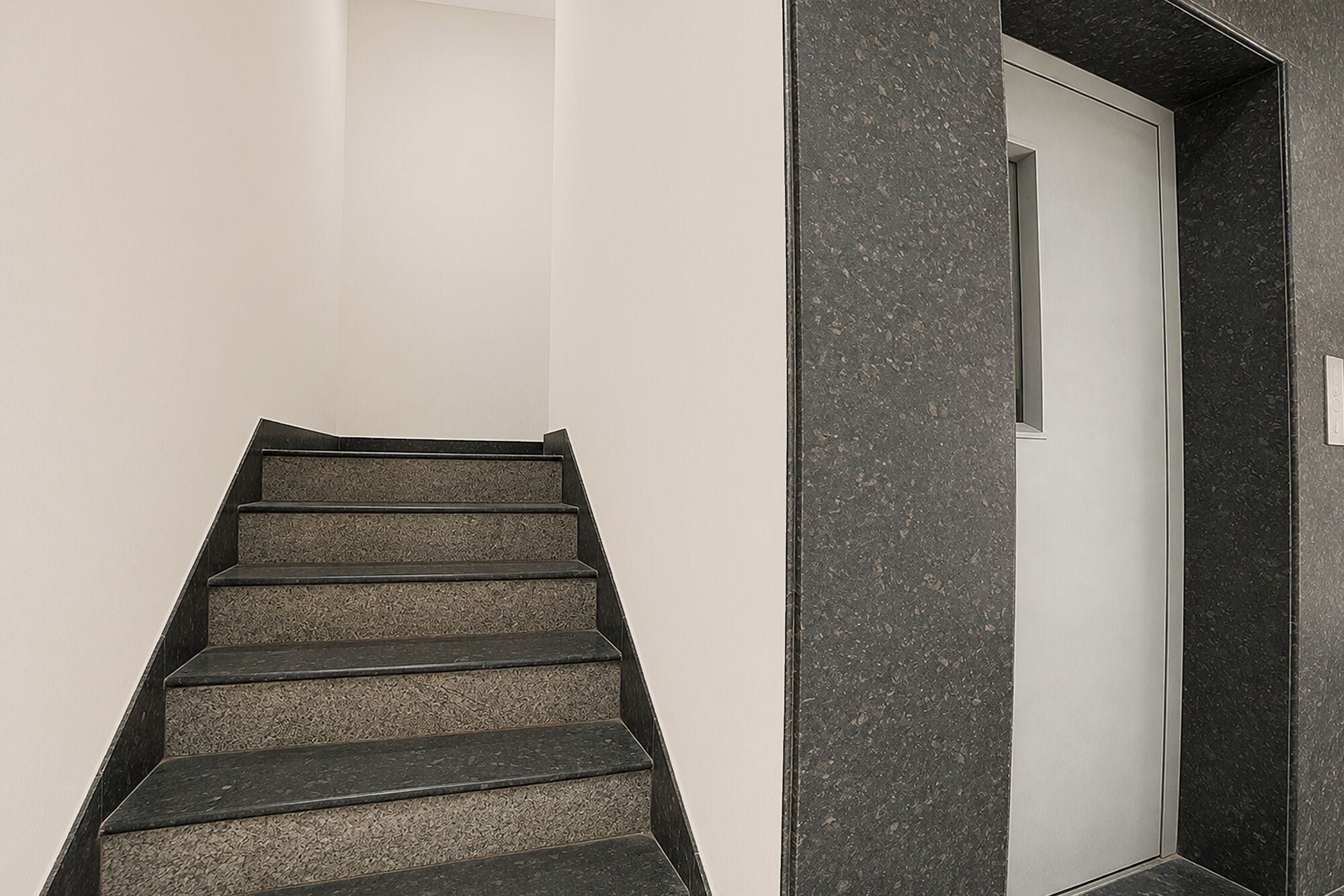 Una escalera de color oscuro que lleva a una puerta blanca.