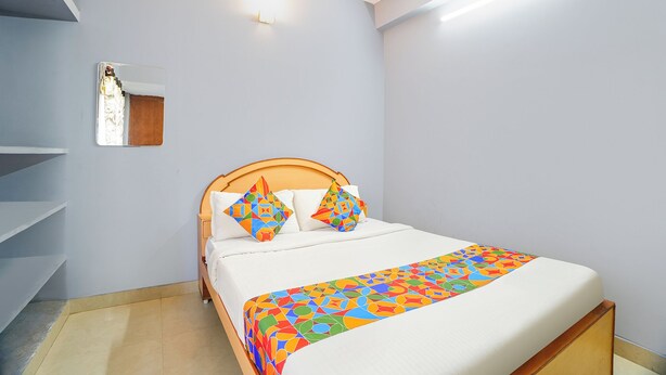A bedroom with a bed, a nightstand, a mirror, and a wall-mounted light fixture.
