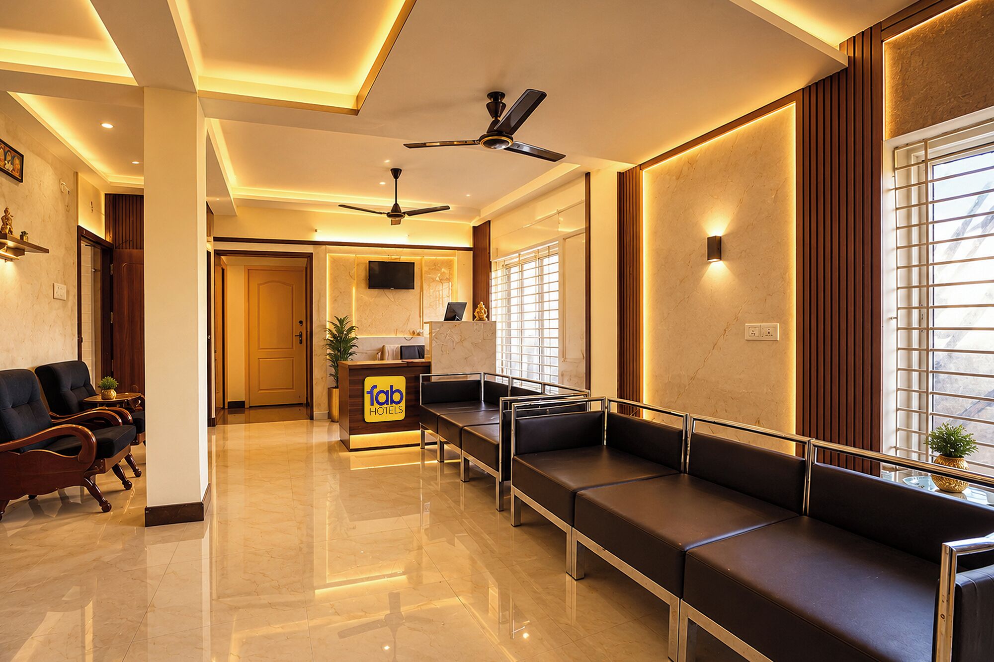 A hotel reception area with a reception desk, seating area, ceiling fans, and a TV mounted on the wall.