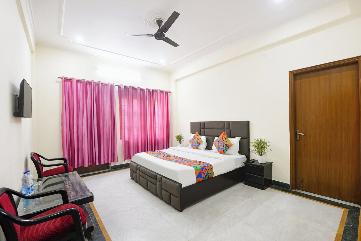 A hotel room with a bed, a desk, chairs, a television, a ceiling fan, and a wooden door.