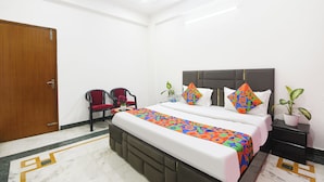 Habitación de hotel con cama, dos sillones, una mesita de noche y una planta en maceta.