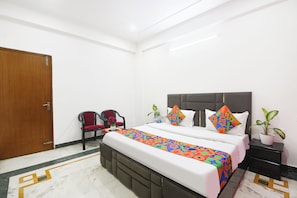 Habitación de hotel con cama, dos sillones, una mesita de noche y una planta en maceta.