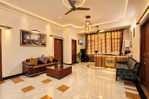A hotel lobby with a reception desk, seating area, and a ceiling fan. - Fabhotel Maurya Residency (Gurugram)