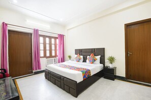 A bedroom with a large bed, a nightstand, a potted plant, and a window with curtains. - FabHotel Maurya Residency (Gurugram)