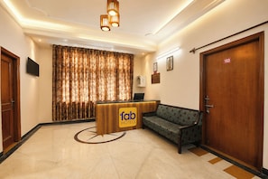 Zona de recepción de un hotel con mostrador, un sofá y una puerta de madera grande.
