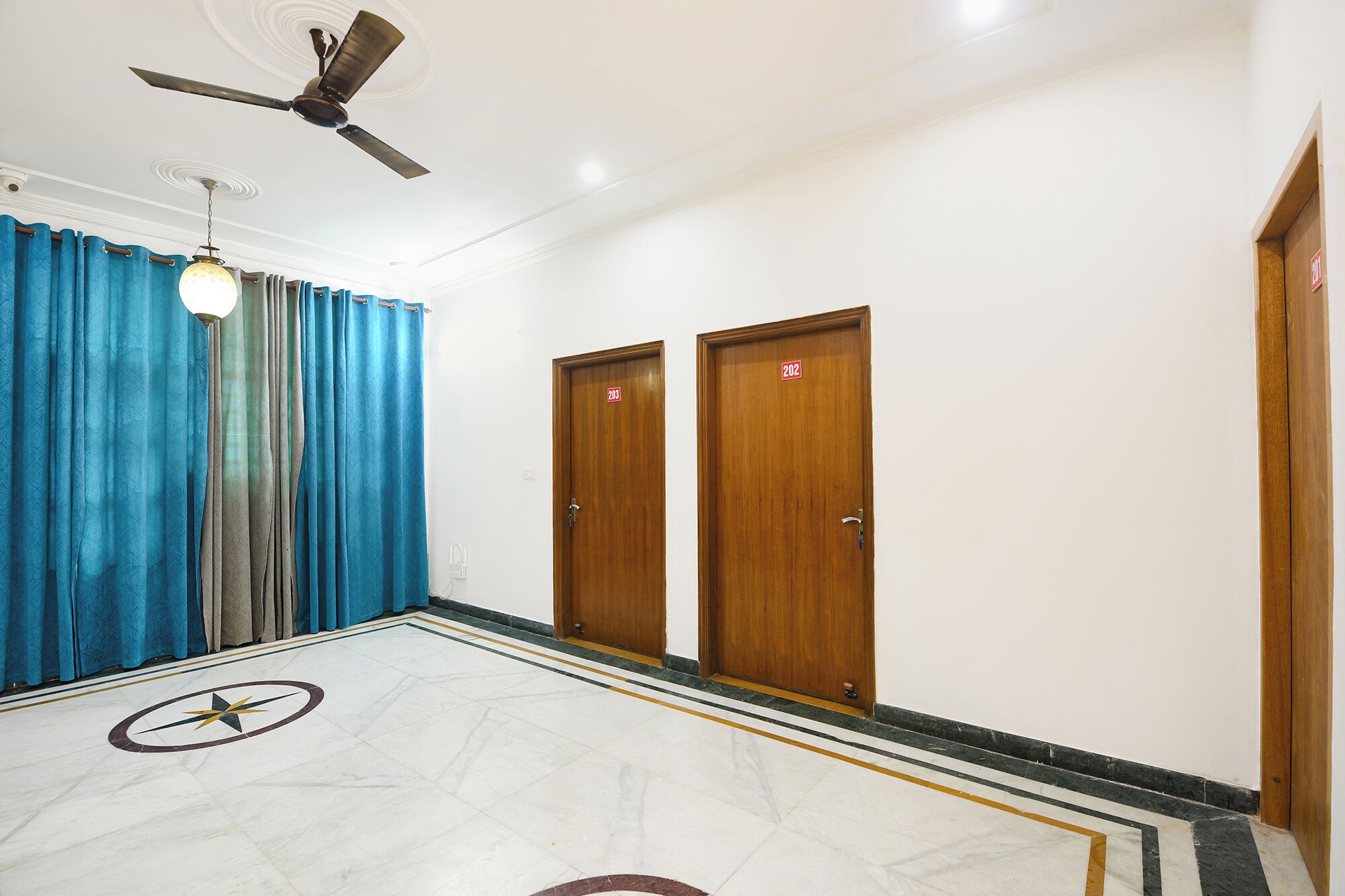 A hotel corridor with a ceiling fan, two wooden doors with room numbers, and a patterned floor.