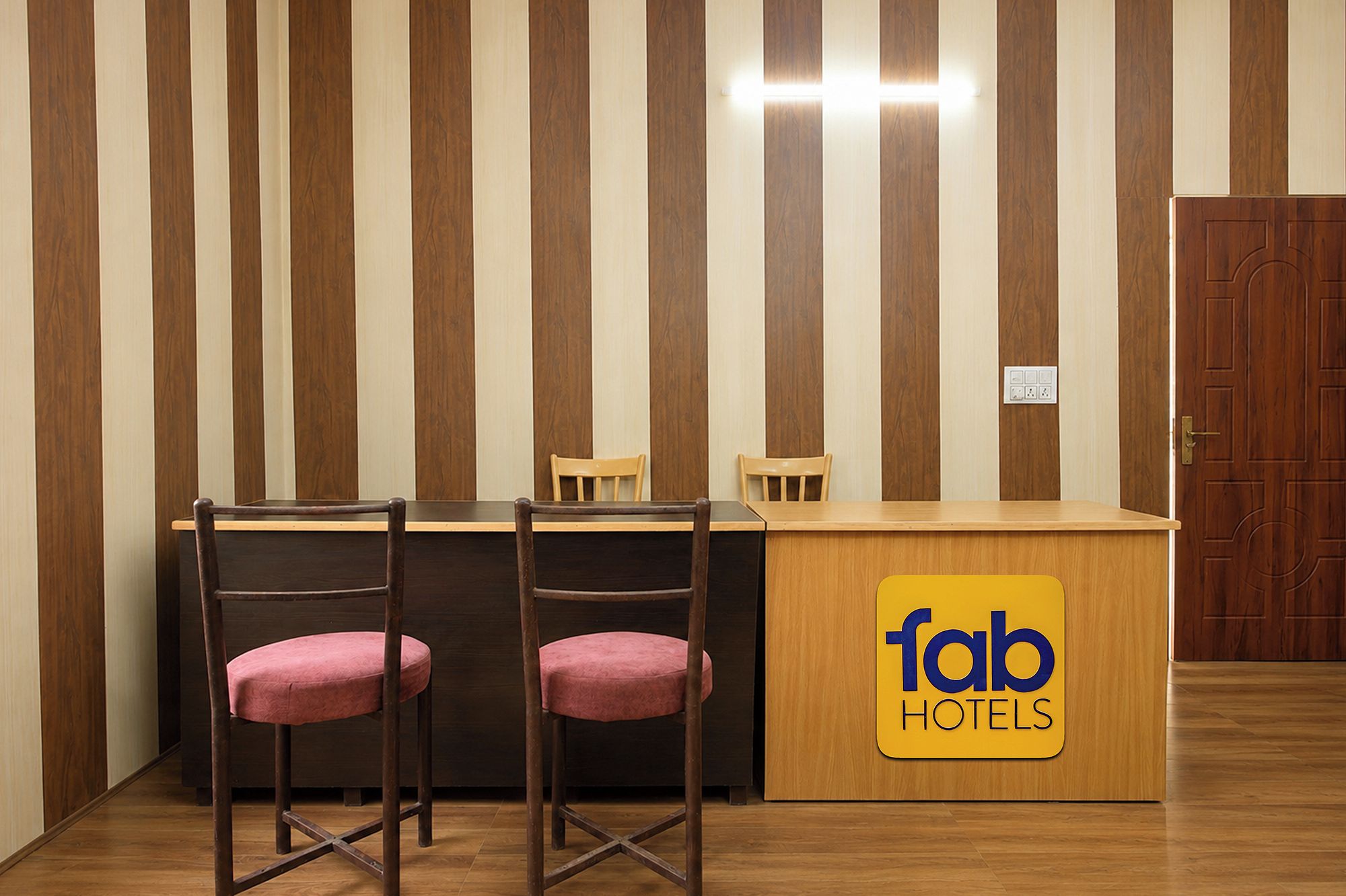 Een hotel receptiebalie met twee houten stoelen, een houten toonbank en een bordje met 'fab hotels'.