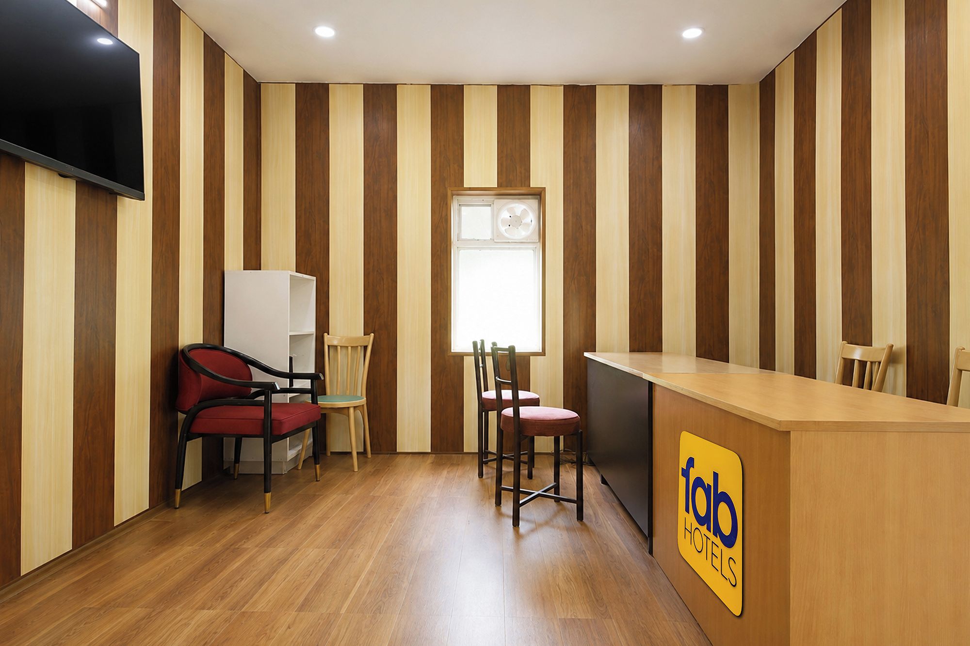 A hotel room with striped wooden walls, a flat-screen TV, a desk with a logo, and two chairs.