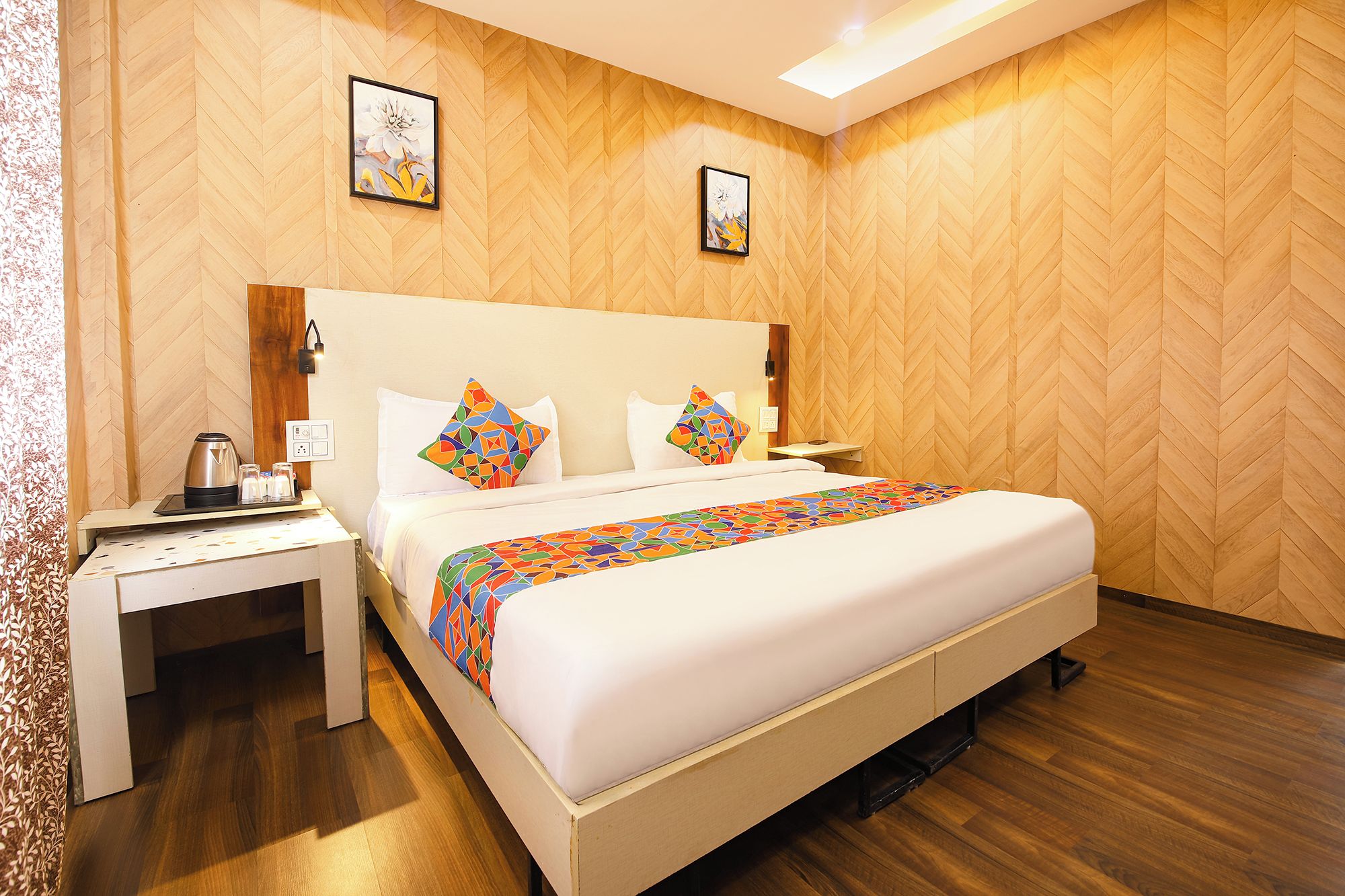 A hotel room with a large bed, two nightstands, a coffee maker, and two framed pictures on the wall.
