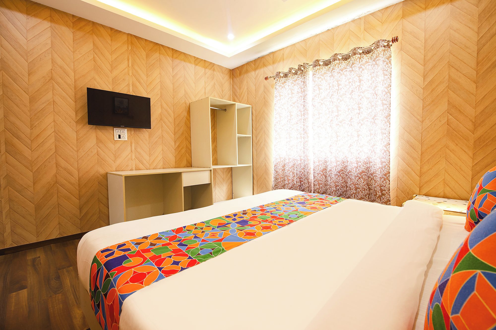 Habitación de hotel con cama, televisor montado en la pared, armario y ventana con cortinas.