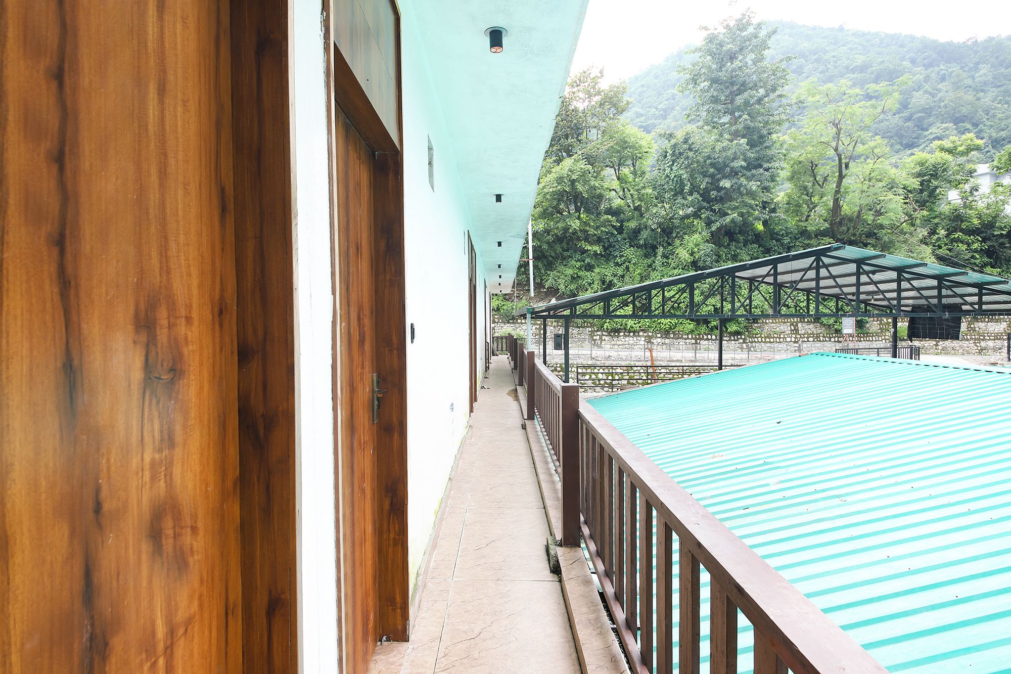 A balcony with a view of a swimming pool and a covered area, overlooking a mountainous landscape.