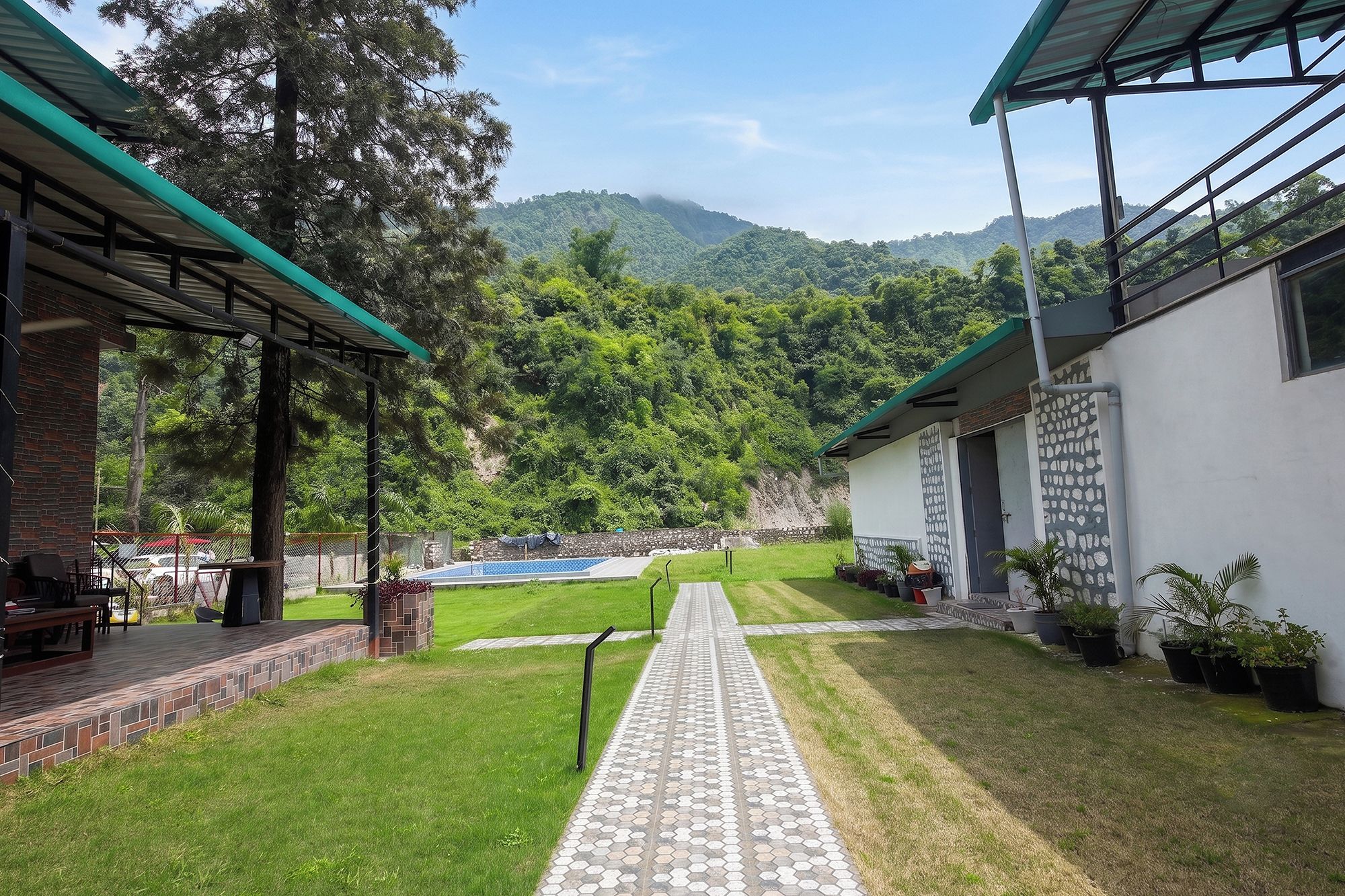 Ein Innenhof mit einem gepflasterten Weg, einem Pool und Blick auf einen bewaldeten Gebirgszug.