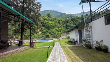 Un patio con sendero empedrado, piscina y vistas a una cadena montañosa boscosa.