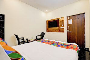 A hotel room with a bed, a desk with two chairs, a television mounted on the wall, and a wooden door. - Fabhotel Sk Grand Banquet (Visakhapatnam)